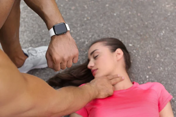 Young man checking pulse of unconscious woman on street — Stock Photo, Image