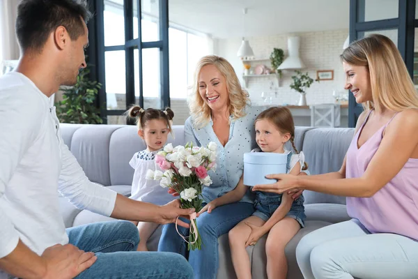 Familia feliz con niños pequeños felicitando a la mujer madura en la sala de estar — Foto de Stock