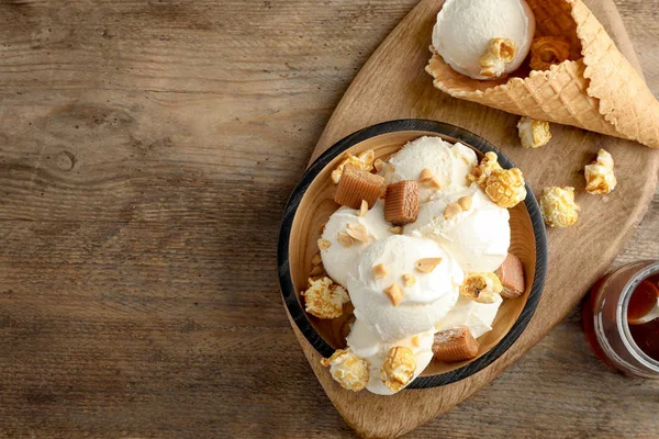 Prato de delicioso sorvete com doces de caramelo e pipoca na mesa de madeira, flat lay. Espaço para texto — Fotografia de Stock