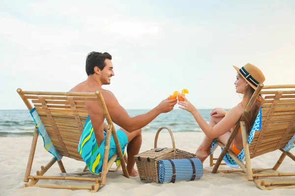 Jovem casal feliz com coquetéis sentados em cadeiras na praia do mar — Fotografia de Stock