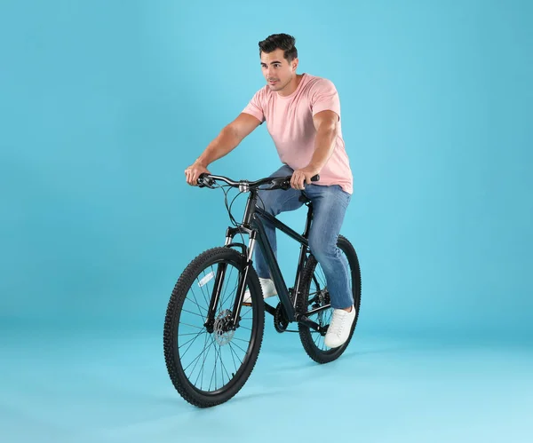 Красивий молодий чоловік з сучасним велосипедом на світло-блакитному тлі — стокове фото
