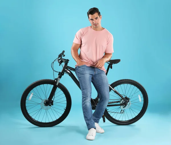 Schöner junger Mann mit modernem Fahrrad auf hellblauem Hintergrund — Stockfoto