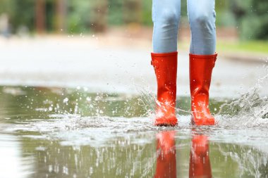 Kırmızı lastik çizmeli kadın su birikintisinde atlıyor, yakın çekim. Yağmurlu hava