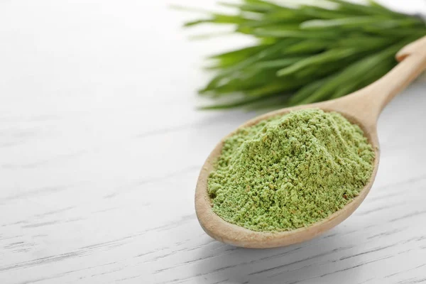 Spoon of wheat grass powder and green sprouts on white wooden table, closeup. Space for text