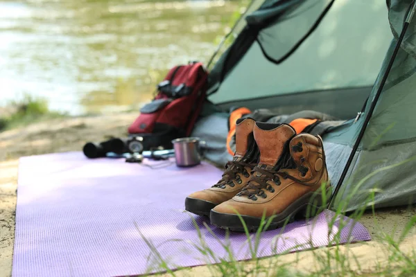 Stövlar och campingutrustning nära tält på Riverbank. Utrymme för text — Stockfoto