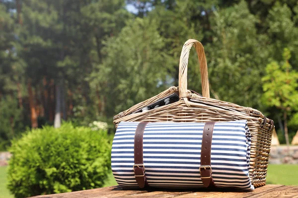 Picknickmand met deken op houten tafel in de tuin — Stockfoto