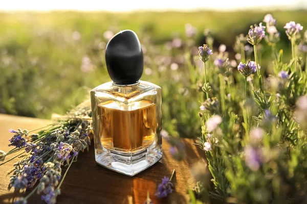 Flasche Luxus-Parfüm und Lavendelblüten auf Holztisch im blühenden Feld — Stockfoto