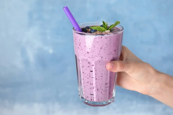 Frau hält Glas leckeren Blaubeer-Smoothie auf blauem Hintergrund, Nahaufnahme — Stockfoto