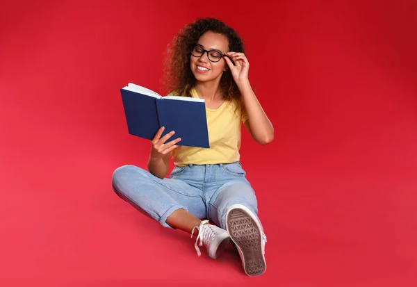 Hermosa joven afroamericana leyendo libro sobre fondo rojo — Foto de Stock