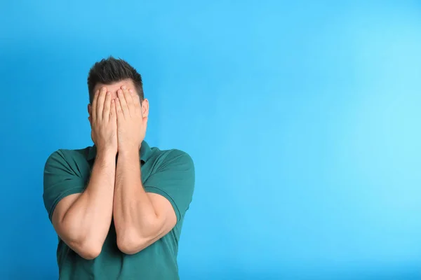 Man covering eyes while being blinded on blue background — Stock Photo, Image