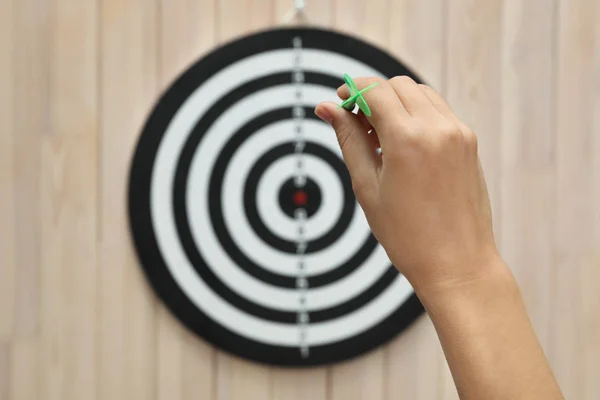 Mujer lanzando flecha verde en tablero de dardos sobre fondo de madera, primer plano —  Fotos de Stock