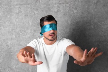 Young man wearing light blue blindfold on grey background clipart
