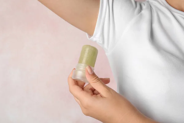 Mujer joven sosteniendo desodorante de alumbre de cristal natural cerca de la axila sobre fondo rosa claro, primer plano —  Fotos de Stock
