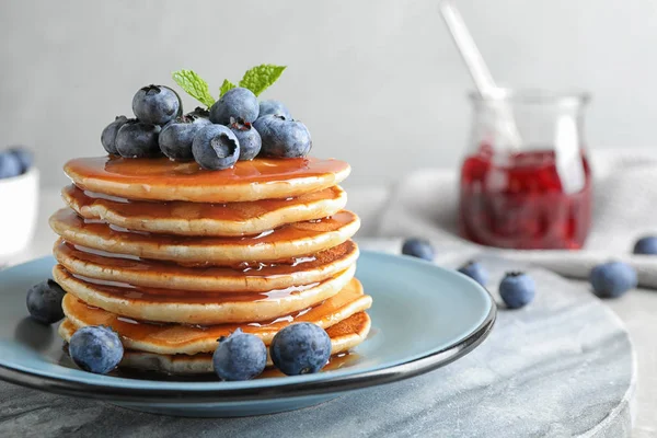 Plate of delicious pancakes with fresh blueberries and syrup on grey table against light background — Stock Photo, Image