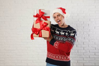 Noel kazak ve Santa şapka beyaz tuğla duvara yakın hediye kutuları tutan Mutlu adam