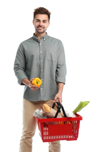 Junger Mann mit Paprika und Einkaufskorb voller Produkte auf weißem Grund — Stockfoto