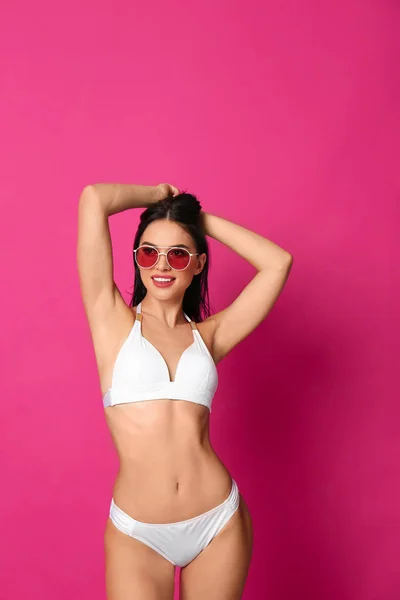 Bella giovane donna in bikini bianco con occhiali da sole su sfondo rosa — Foto Stock