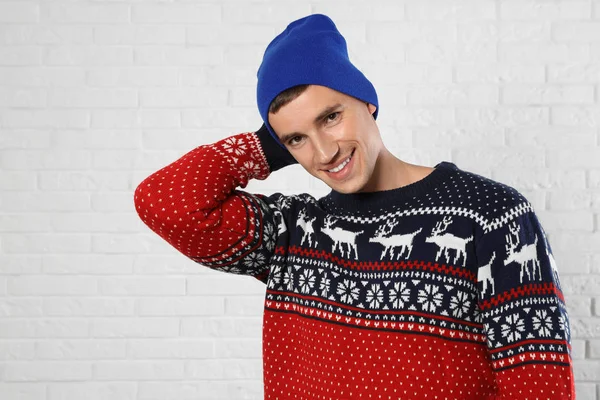 Portrait of young man in Christmas sweater and hat near white brick wall — Stock Photo, Image