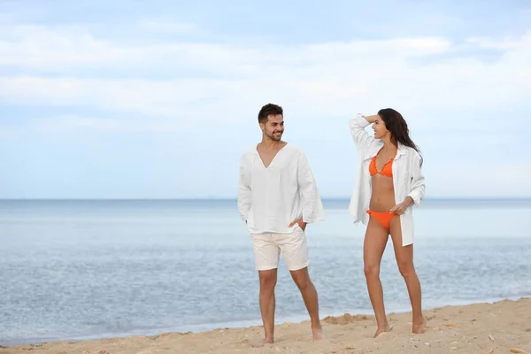 Feliz joven pareja caminando juntos en la playa cerca del mar —  Fotos de Stock