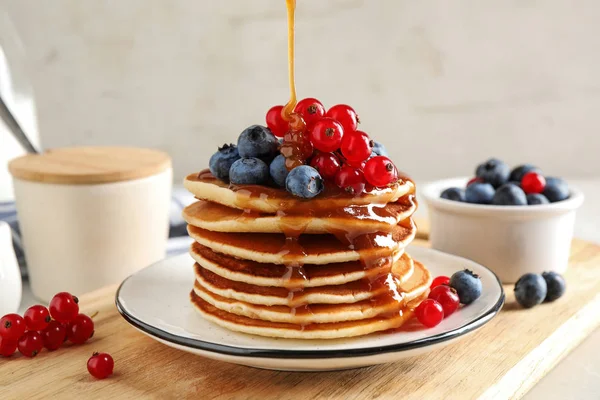 Menuang sirup ke pancake dengan buah berry segar di atas meja — Stok Foto