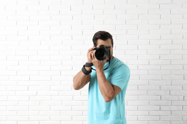 Jovem fotógrafo profissional tirando fotos perto da parede de tijolo. Espaço para texto — Fotografia de Stock