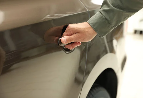 Hombre joven abriendo la puerta del coche en concesionario de automóviles modernos, primer plano — Foto de Stock