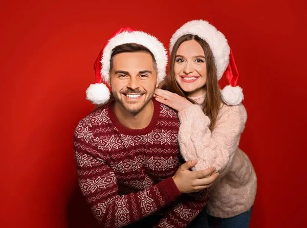 Coppia che indossa maglioni di Natale e cappelli di Babbo Natale su sfondo rosso — Foto Stock