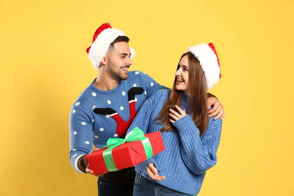 Casal usando camisolas de Natal e chapéus de Papai Noel no fundo amarelo — Fotografia de Stock