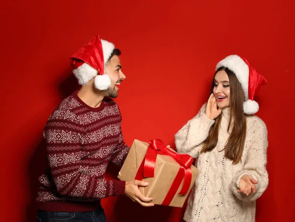 Couple portant des pulls de Noël et des chapeaux de Père Noël sur fond rouge — Photo