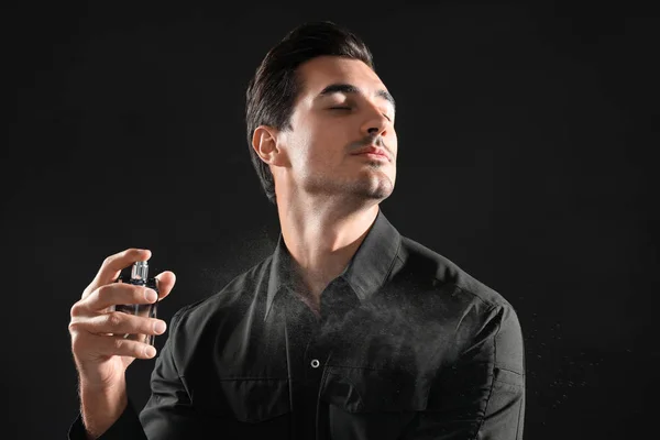 Handsome young man applying perfume on black background — Stock Photo, Image