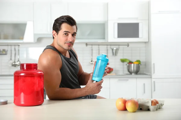 Homem atlético jovem com ingredientes para batido de proteína na cozinha, espaço para texto — Fotografia de Stock