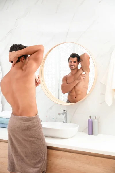 Beau jeune homme appliquant déodorant dans salle de bain — Photo