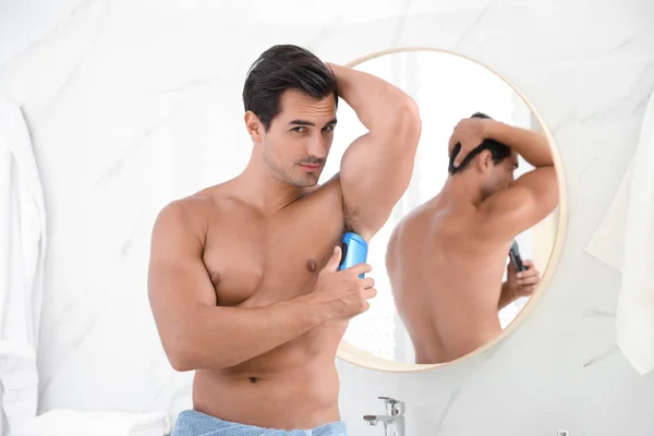 Handsome young man applying deodorant in bathroom