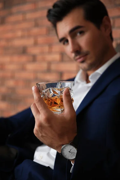 Jeune homme avec un verre de whisky près d'un mur de briques à l'intérieur — Photo