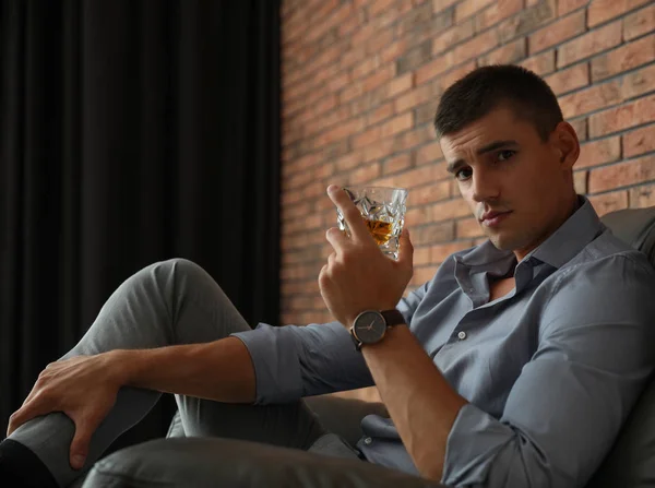 Jeune homme avec un verre de whisky près d'un mur de briques à l'intérieur — Photo