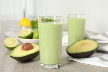 Ahşap masa üzerinde lezzetli avokado smoothie ve malzemelerle dolu camlar