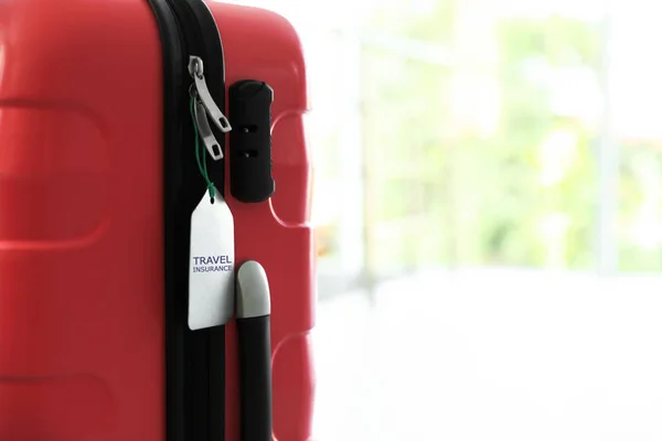 Elegante maleta con etiqueta de seguro de viaje sobre fondo borroso, primer plano. Espacio para texto —  Fotos de Stock