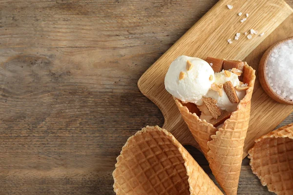 Вафельный рожок с мороженым, карамелью и орехами на деревянном столе, вид сверху. Пространство для текста — стоковое фото