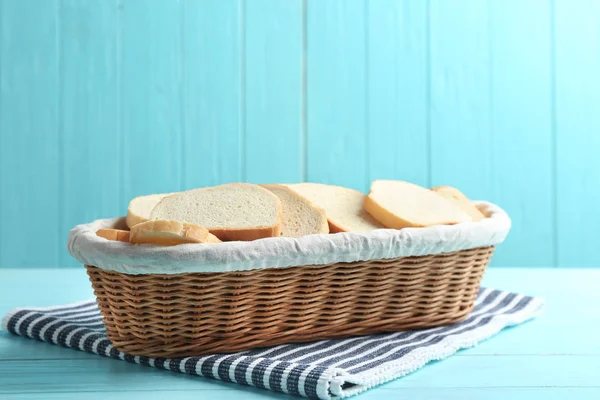 Fette di pane fresco saporito in cesto di vimini su tavolo di legno azzurro — Foto Stock