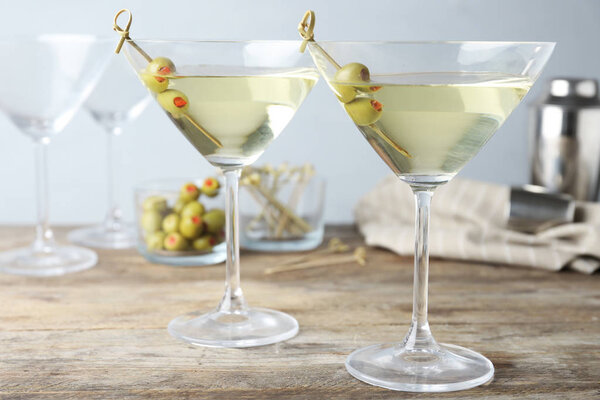 Glasses of Classic Dry Martini with olives on wooden table against grey background
