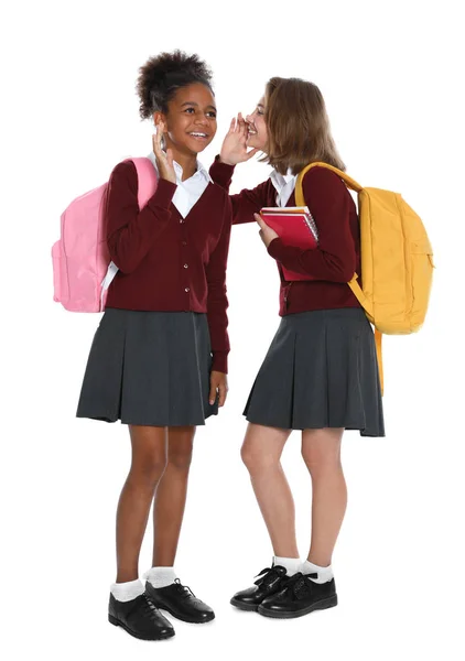 Glückliche Mädchen in Schuluniform tratschen auf weißem Hintergrund — Stockfoto