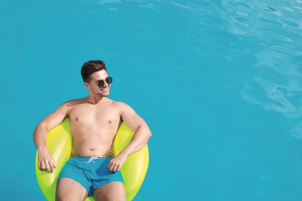 Joven guapo con anillo inflable en la piscina en el día soleado, sobre la vista. Espacio para texto — Foto de Stock