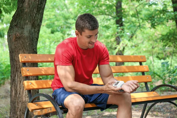 Genç adam parkta bankta eğitim den sonra tıbbi cihaz ile nabız kontrol