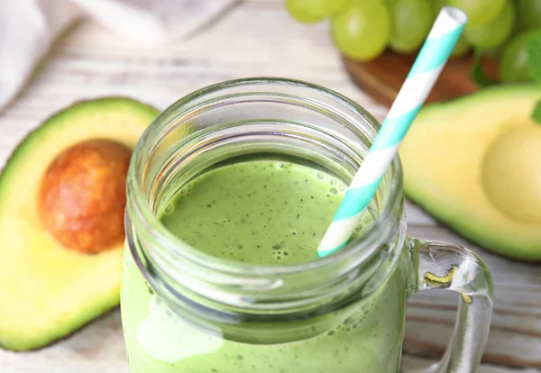 Mason jar van smakelijke avocado smoothie met stro op tafel, close-up — Stockfoto