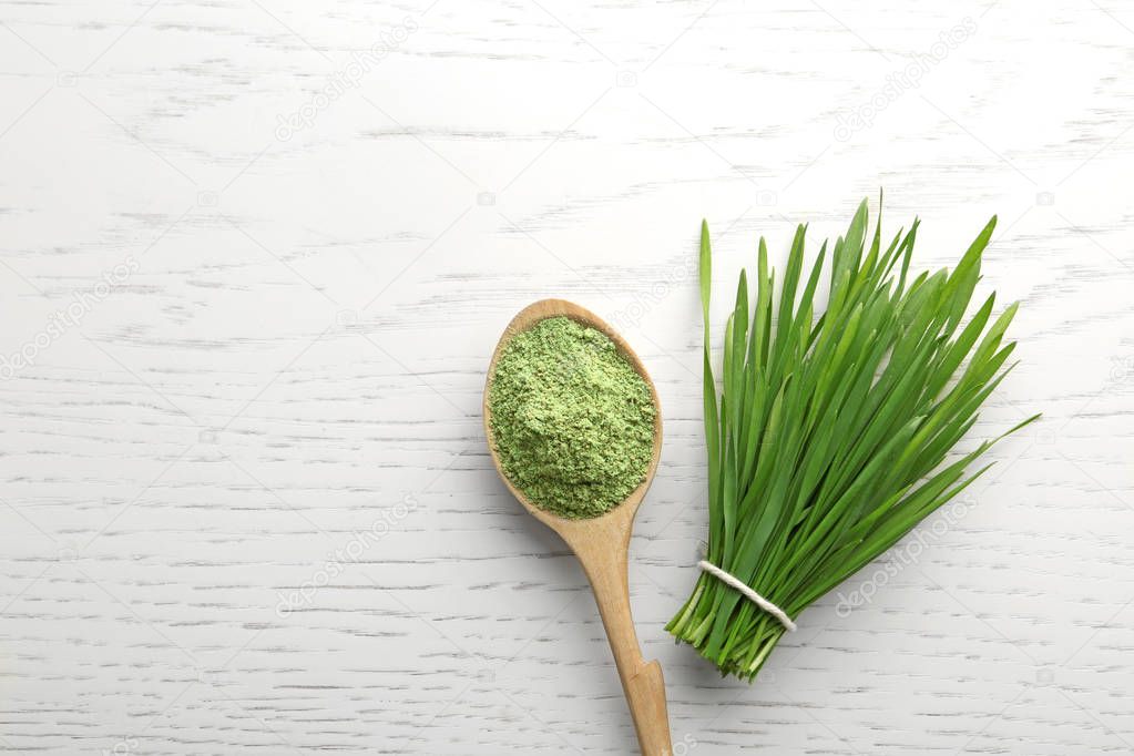 Spoon of wheat grass powder and green sprouts on white wooden table, flat lay. Space for text
