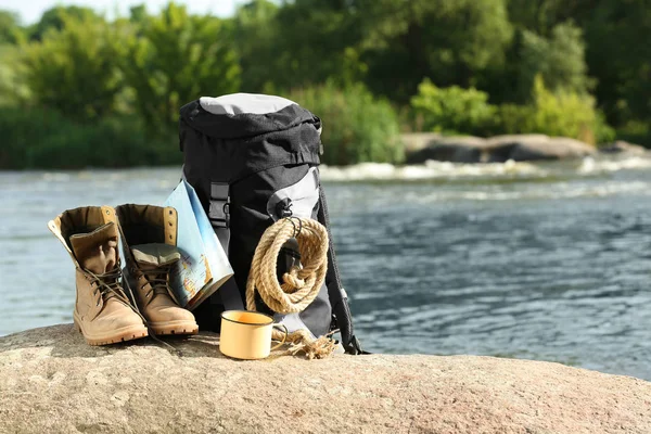 Backpack and camping equipment on rock near river. Space for text