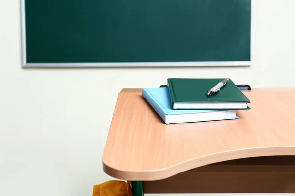 Drewniane biurko szkolne z papeterią w pobliżu tablica w klasie — Zdjęcie stockowe