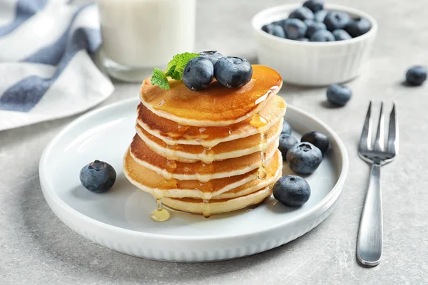 Plate of tasty pancakes with blueberries and honey on light grey table — Stock Photo, Image