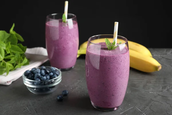 Gläser leckerer Blaubeer-Smoothie auf grauem Tisch vor schwarzem Hintergrund — Stockfoto