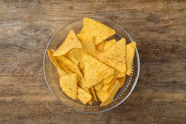 Glass bowl with tasty Mexican nachos chips on wooden table, top view — Stock Photo, Image